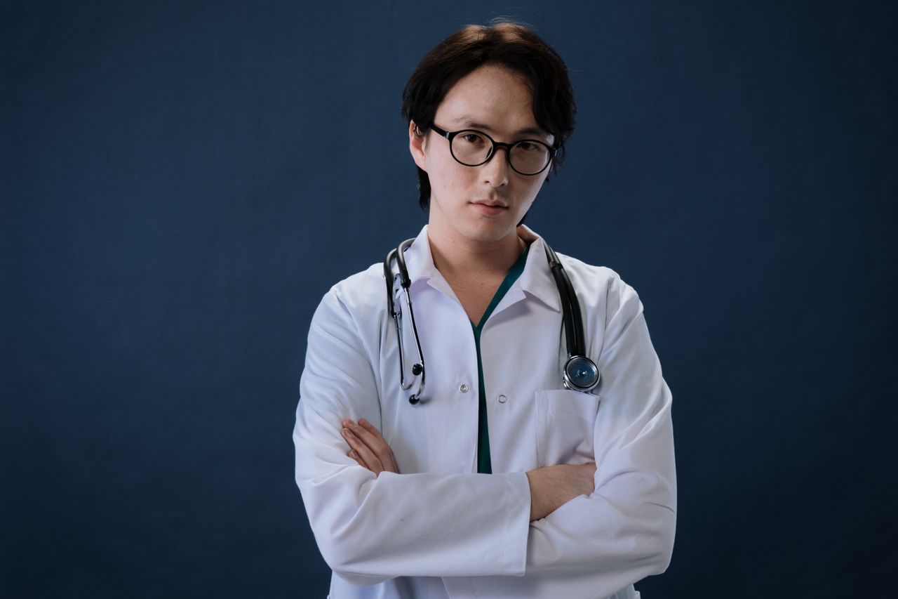 Offerings Portrait of a doctor with eyeglasses and stethoscope against a blue background in professional attire.